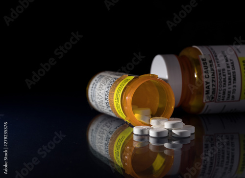 Oxycodone is the generic name for a range of opoid pain killing tablets. Prescription bottle for Oxycodone tablets and pills on glass table with reflections