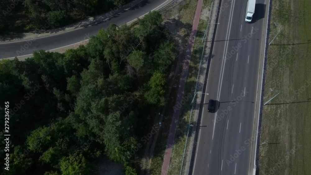 Cars are moving on the highway surrounded by green trees in the summer.