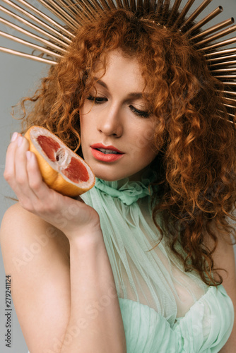 redhead woman with accessory on head posing with grapefruit on grey