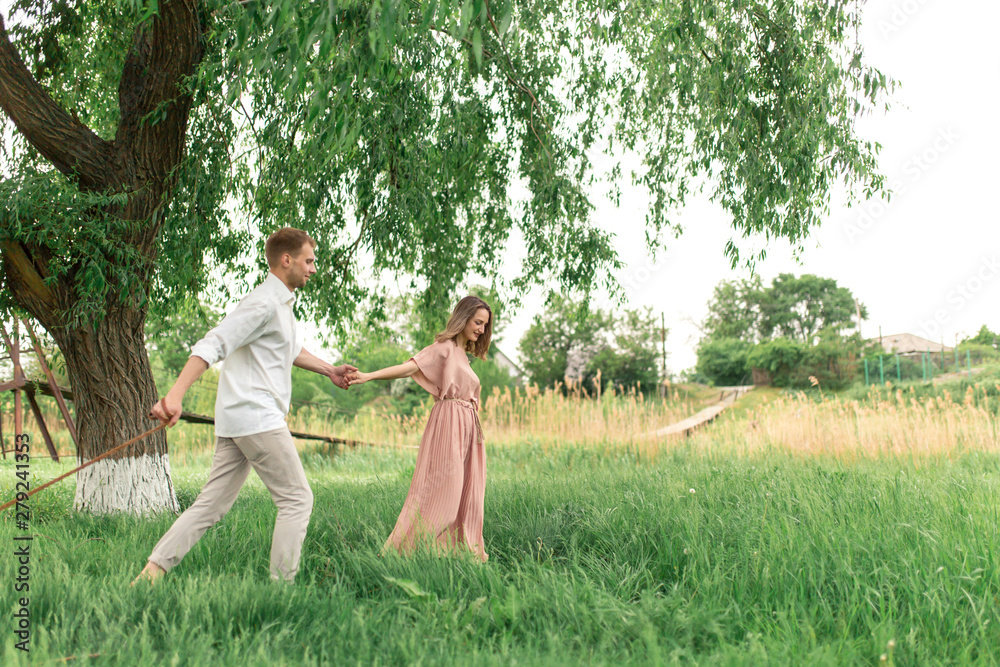 Obraz premium Young loving couple having fun and running on the green grass on the lawn with their beloved domestic dog breed Beagle and a bouquet of wildflowers