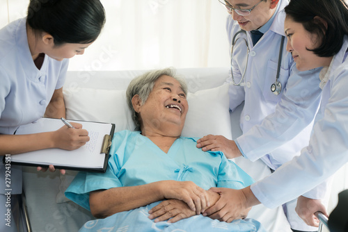 Asian medical team of doctors examining and talking to ASian elderly woman patient, health care people take note on clipboard in hospital.