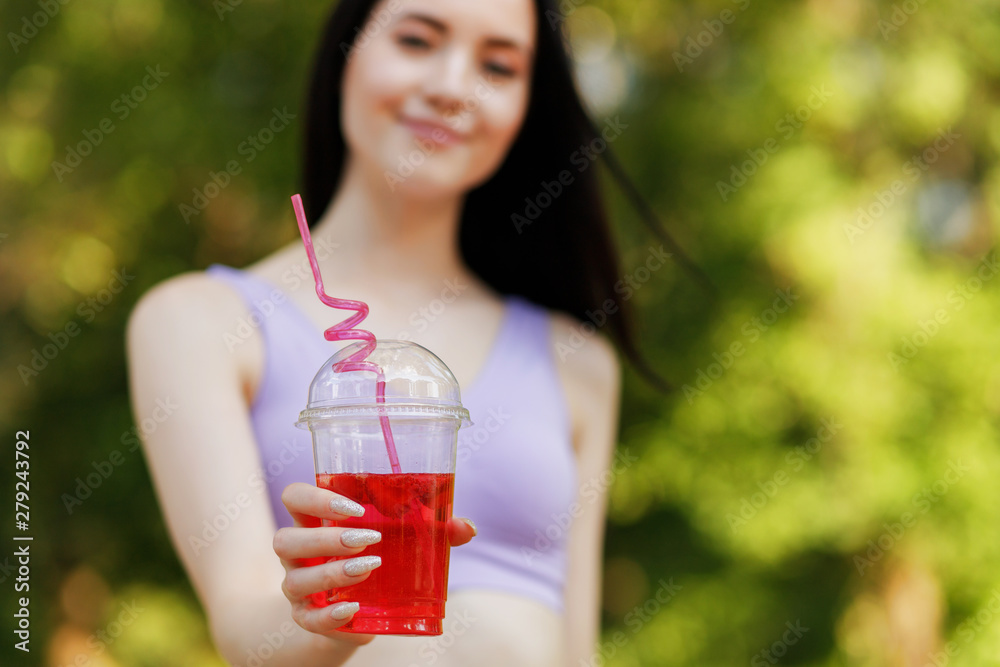 Young beautiful girl drinking fresh juice from plastic cup take-out food. Smiling slim brunette woman with berry lemonade in park. Summer cold drinks. Young beautiful girl drinking fresh juice from plastic cup take-out food. Smiling slim brunette woman with berry lemonade in park. Summer cold drinks.