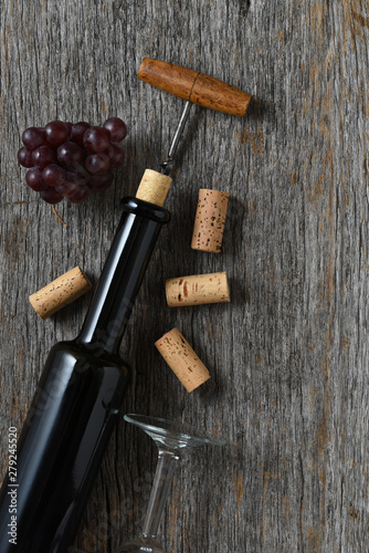 Wine bottle on rustic wood tabnle with the cork pulled partially out, with grapes and corks