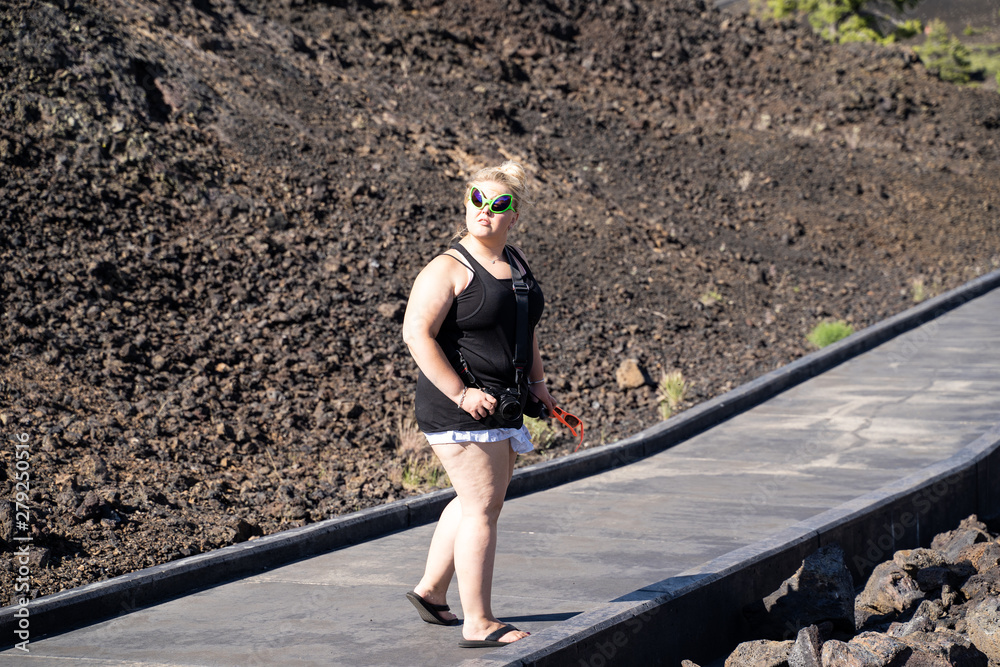 Blonde woman wearing alien sunglasses walks on a boardwalk in Craters of the Moon National Monument in Idaho. Concept for extraterrestrial - obrazy, fototapety, plakaty 