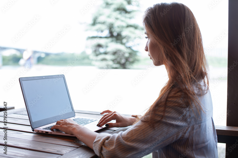 Naklejka premium Young sensitive woman using laptop computer in the street cafe outdoor. Freelance work concept. Summer restaurant outdoor. Learning foreign languages online. Lesson with tutor. Typing on a keyboard.