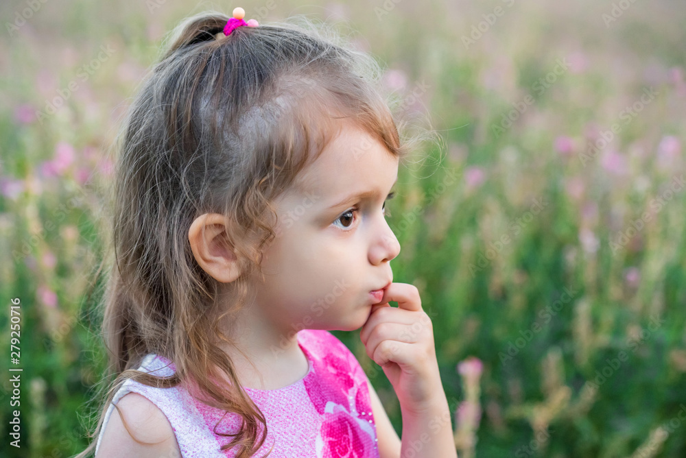 Cute serious baby girl looks aside outdoors in green field. Child portrait Cute serious baby girl looks aside outdoors in green field. Child portrait