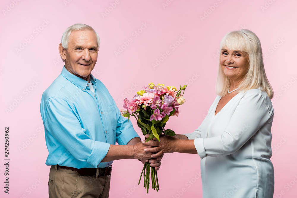 cheerful senior man giving bouquet with flowers to happy retired wife on pink cheerful senior man giving bouquet with flowers to happy retired wife on pink