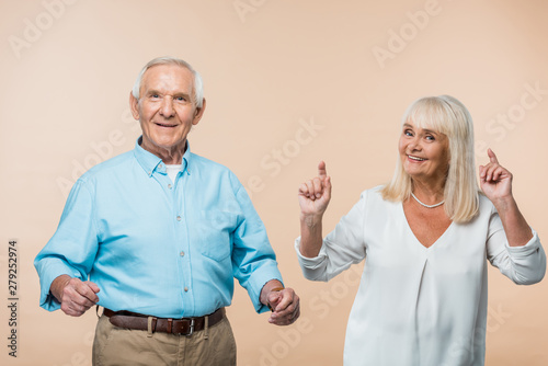 happy retired woman pointing with fingers near husband on beige