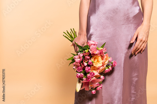 Fototapeta Naklejka Na Ścianę i Meble -  partial view of elegant woman in violet satin dress holding bouquet of flowers isolated on beige