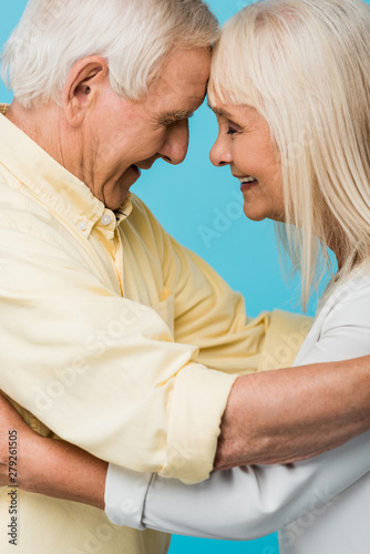 side view of happy retired couple with closed eyes smiling isolated on blue