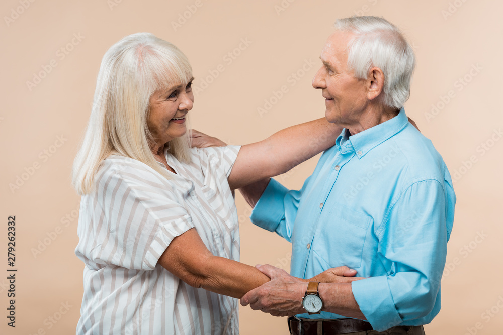 Obraz premium senior woman smiling while looking at pensioner isolated on beige