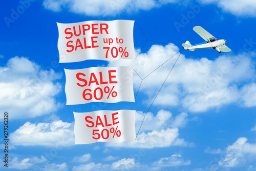 Small airplane towing banner with SALE caption in the sky. Airplane with banners. Advertisement concept.