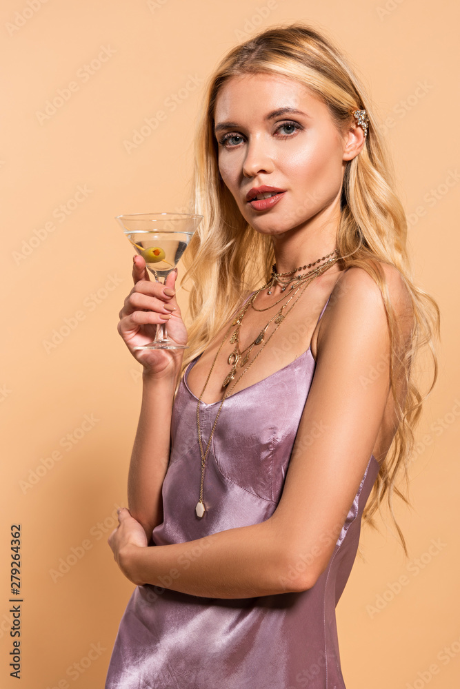 elegant blonde woman in violet satin dress and necklace holding cocktail isolated on beige elegant blonde woman in violet satin dress and necklace holding cocktail isolated on beige