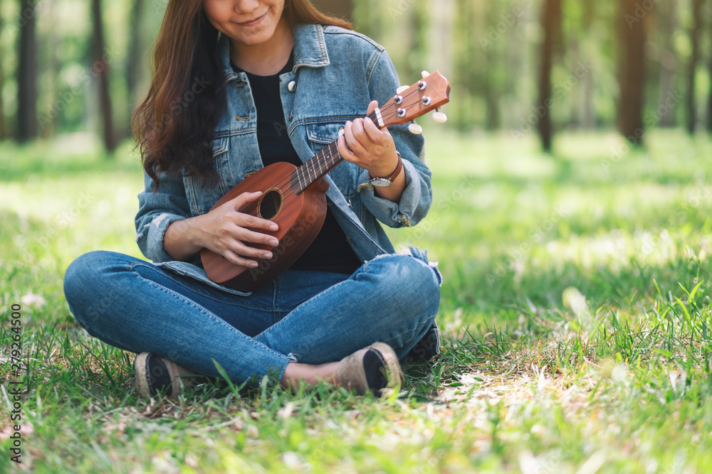 A beautiful asian woman sitting and playing ukulele in the outdoors