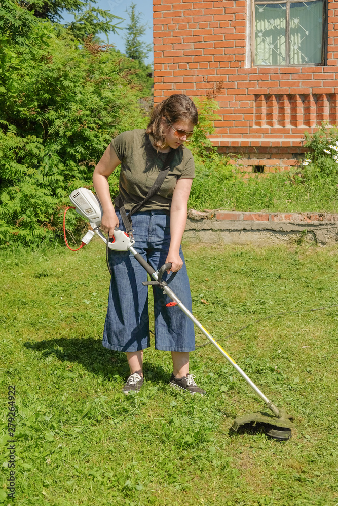 Woman mows the grass trimmer. Portrait of a close-up hand mowing grass. Cut the lawn. Woman mows the grass trimmer. Portrait of a close-up hand mowing grass. Cut the lawn.