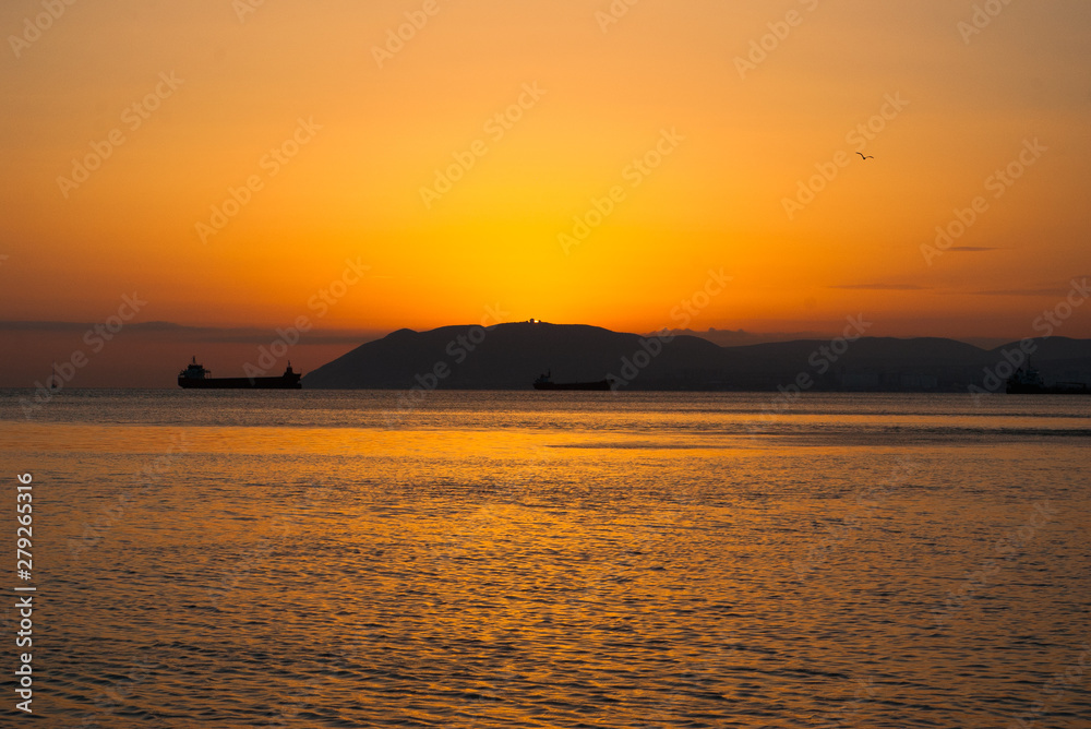 Sunset in Black sea, photographed in Crimea. Several boats sailing on horizon. Water surface rippling. Setting sun kindle clear sky. Evening seascape. Selective soft focus. Blurred background