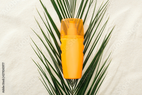 orange sunscreen lotion on green palm leaf on sand