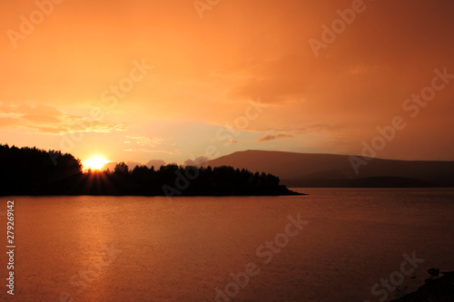 red and orange clouds at sunset over a mountain lake