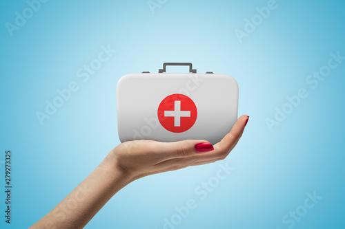 Side closeup of woman's hand facing up and holding small medical bag on light blue gradient background. photo