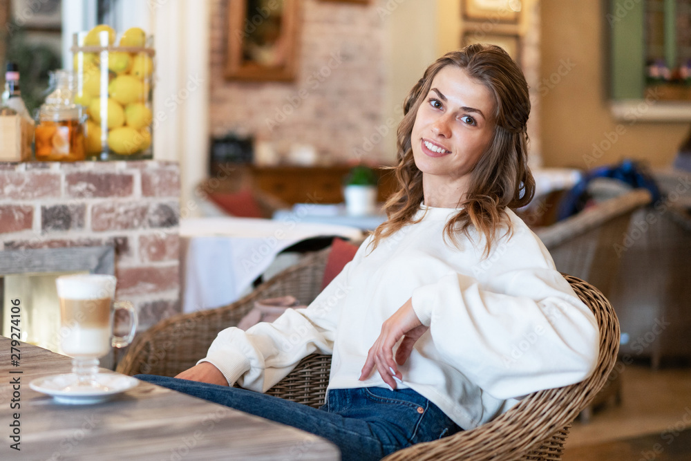 Young caucasian girl sitting in cafe with coffee and dreamily looking around. Young caucasian girl sitting in cafe with coffee and dreamily looking around.