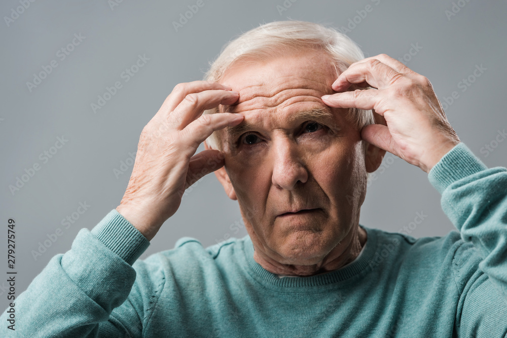 exhausted retired man looking at camera and touching head isolated on grey
