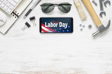 Table top view of labor day abstract background concept. Flat lay mockup smartphone with Happy Labor Day USA Holiday and essential worker tools on grunge white wood background with copy space.