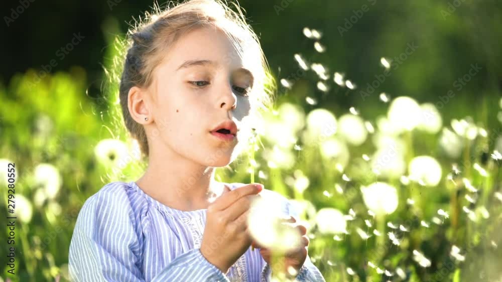 Beautiful little girl at sunny summer day blowing dandelion on green meadow. Summer fun concept. Slow motion. Beautiful little girl at sunny summer day blowing dandelion on green meadow. Summer fun concept. Slow motion.