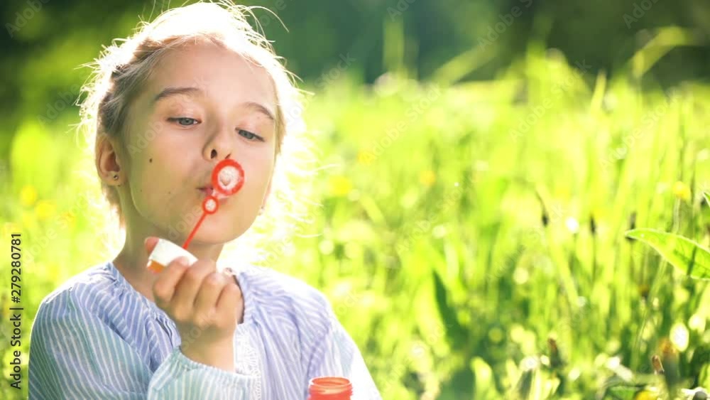 Beautiful little girl at sunny summer day blowing soap bubbles green meadow. Summer fun concept. Slow motion. Beautiful little girl at sunny summer day blowing soap bubbles green meadow. Summer fun concept. Slow motion.