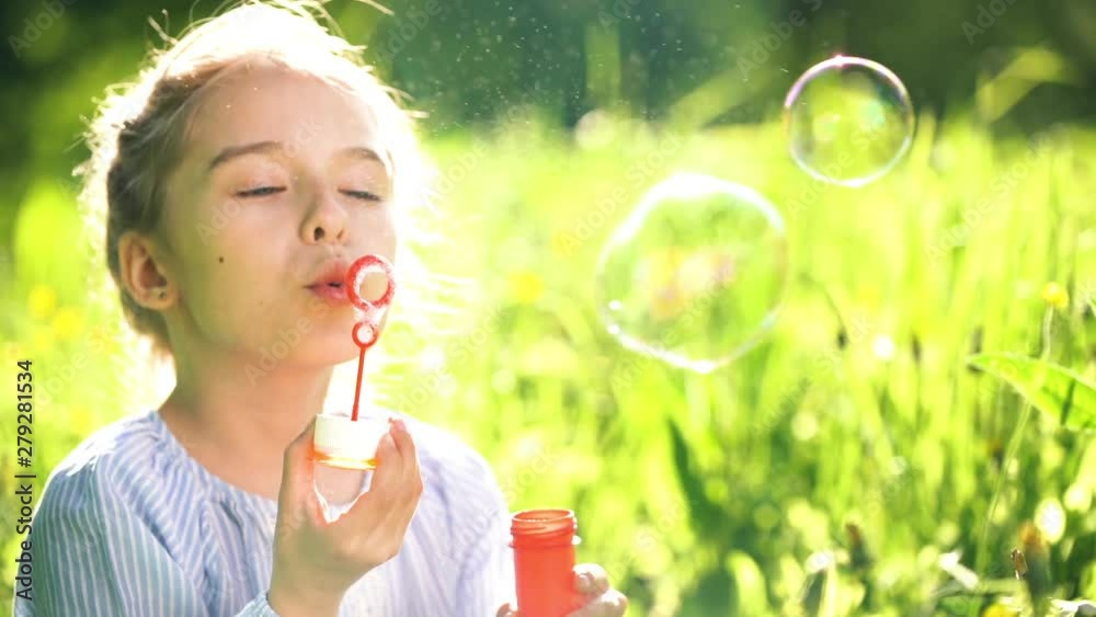 Beautiful little girl at sunny summer day blowing soap bubbles green meadow. Summer fun concept. Slow motion. Beautiful little girl at sunny summer day blowing soap bubbles green meadow. Summer fun concept. Slow motion.