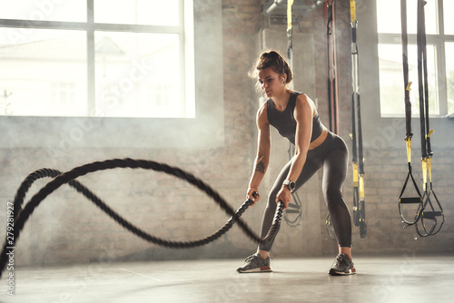 Preparing for the competition. Young athletic woman with perfect body doing crossfit exercises with a rope in the gym. photo