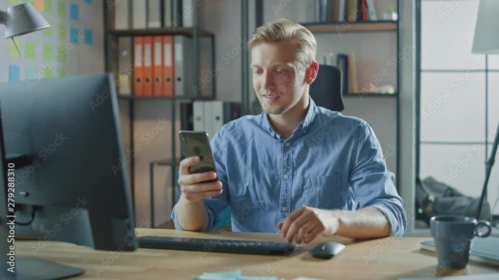 Creative Entrepreneur Sitting at His Desk Works on Desktop Computer in the Stylish Office, Picks up and Starts Using Smartphone, Uses Social Media App, Emailing Business Partners, Messaging Friends Creative Entrepreneur Sitting at His Desk Works on Desktop Computer in the Stylish Office, Picks up and Starts Using Smartphone, Uses Social Media App, Emailing Business Partners, Messaging Friends