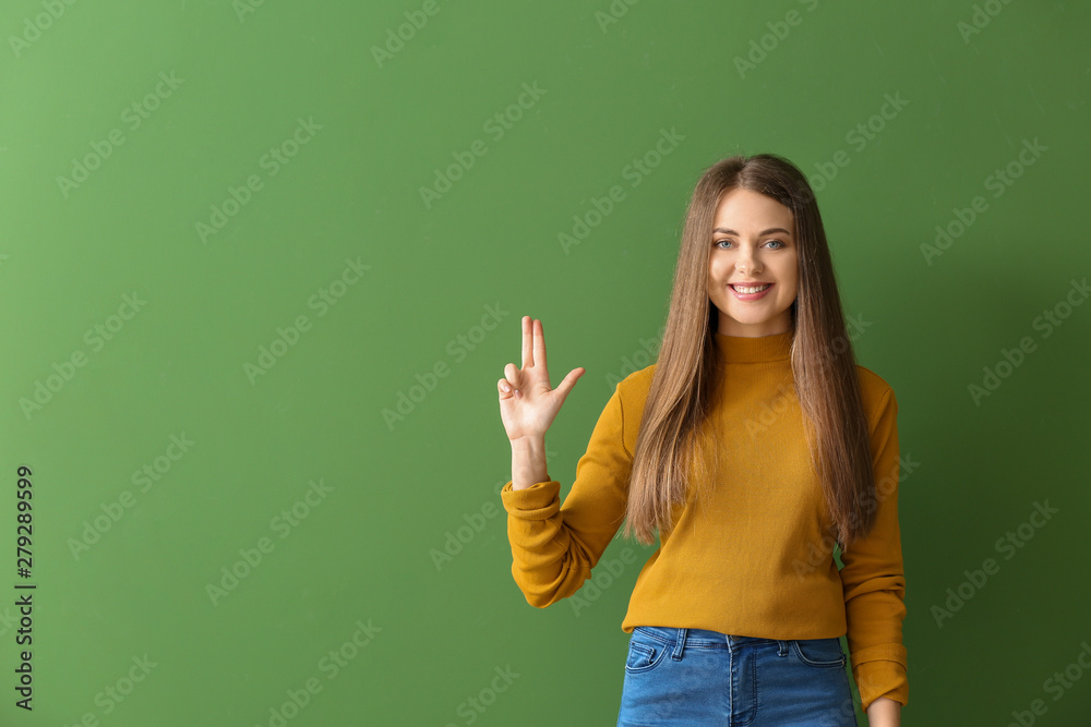 Young deaf mute woman using sign language on color background