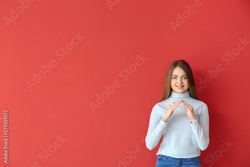 Young deaf mute woman using sign language on color background photo