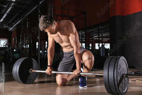 Sporty young man training with barbell in gym