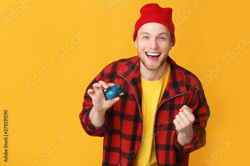 Happy young man with credit card on color background