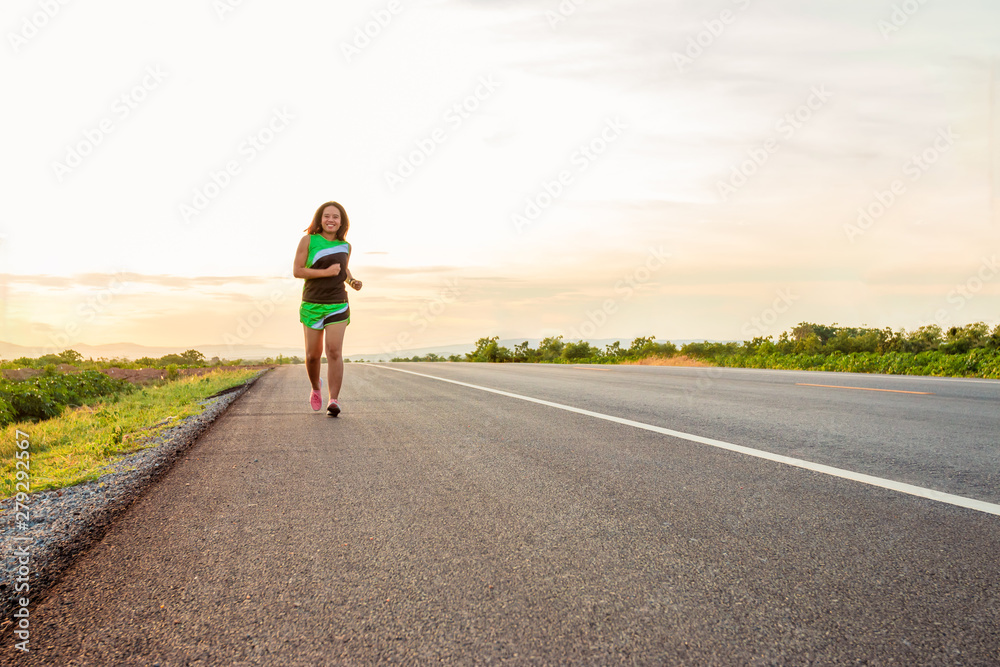 Fototapeta premium Along the road in the hillside area at the time of the sun set woman is exercising by running.
