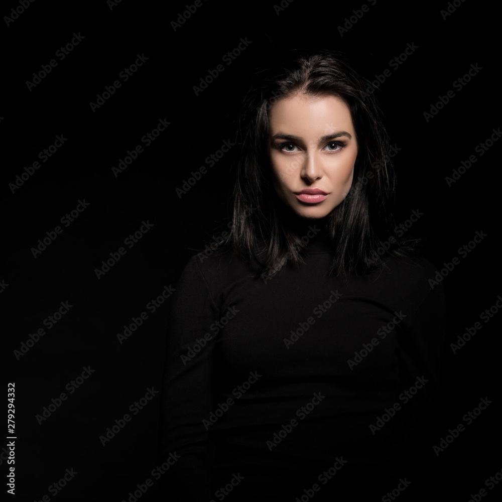 Beautiful girl with dark hair posing over black background. Young pretty woman in studio.
