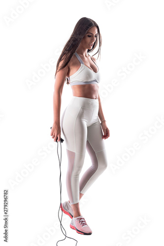 Exhausted sporty woman cardio trainer looking down and holding skipping jump rope. Full body isolated on white background. 