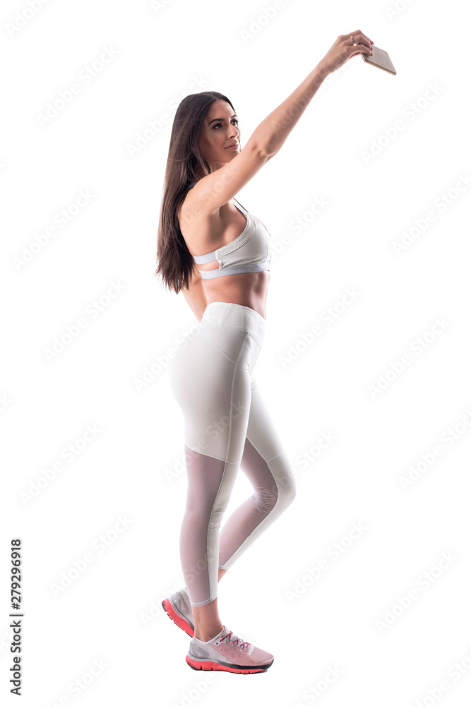 Side view of confident happy fitness woman with athletic body taking selfie with smart phone. Full body isolated on white background. Side view of confident happy fitness woman with athletic body taking selfie with smart phone. Full body isolated on white background.