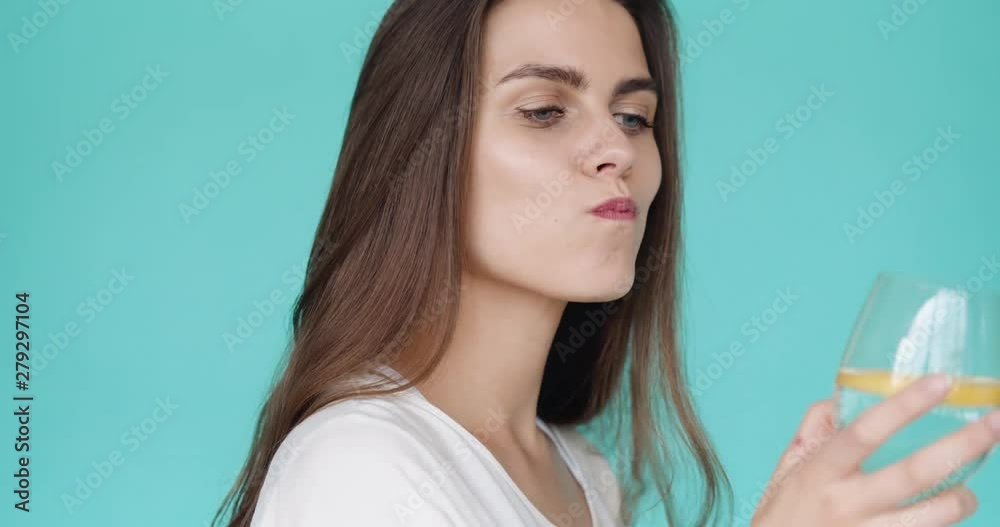Young brunette drinks lemonade. Close-up. Slow motion. Turquoise background. Young brunette drinks lemonade. Close-up. Slow motion. Turquoise background.