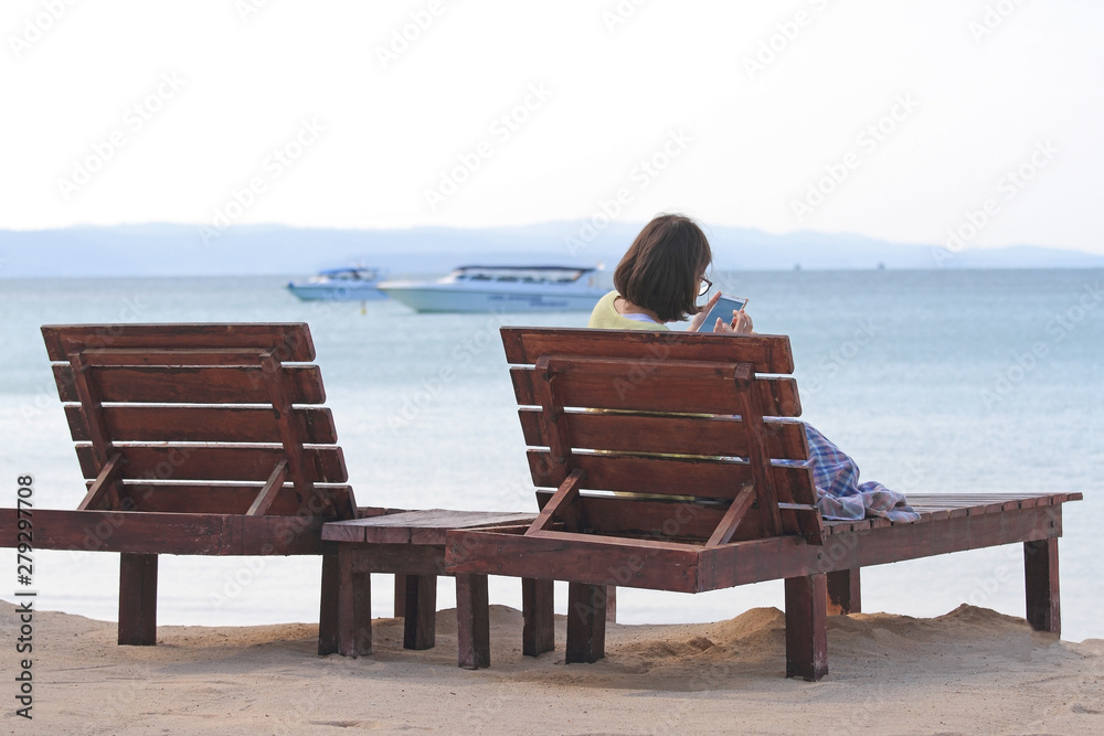 Woman sitting play phone on sun chair with sea view on beach