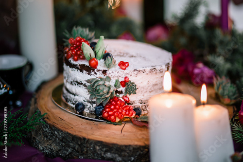 Delicate wedding white cake decorated with pomegranate and succulent surrounded by flowers and candles.