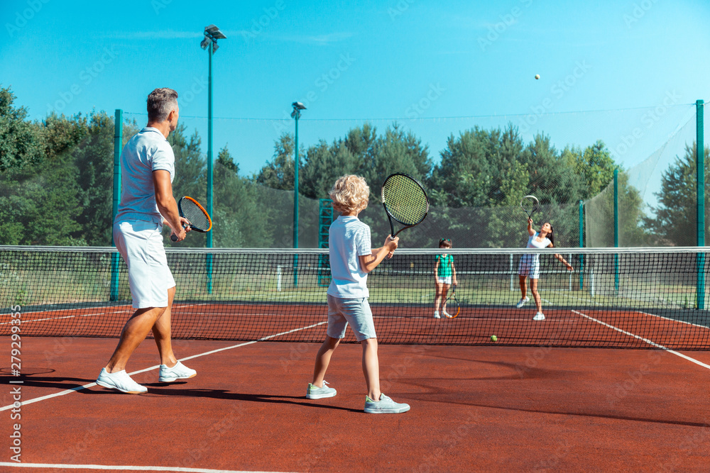 Father and son playing tennis against mother and daughter