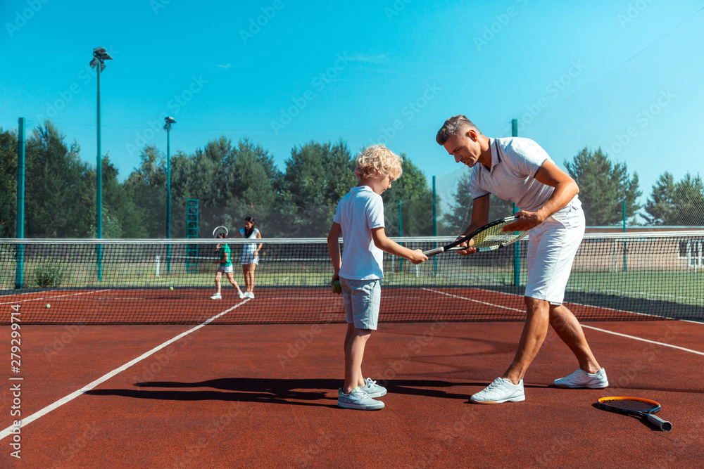 Father wearing white t-shirt giving tennis racket to his cure son