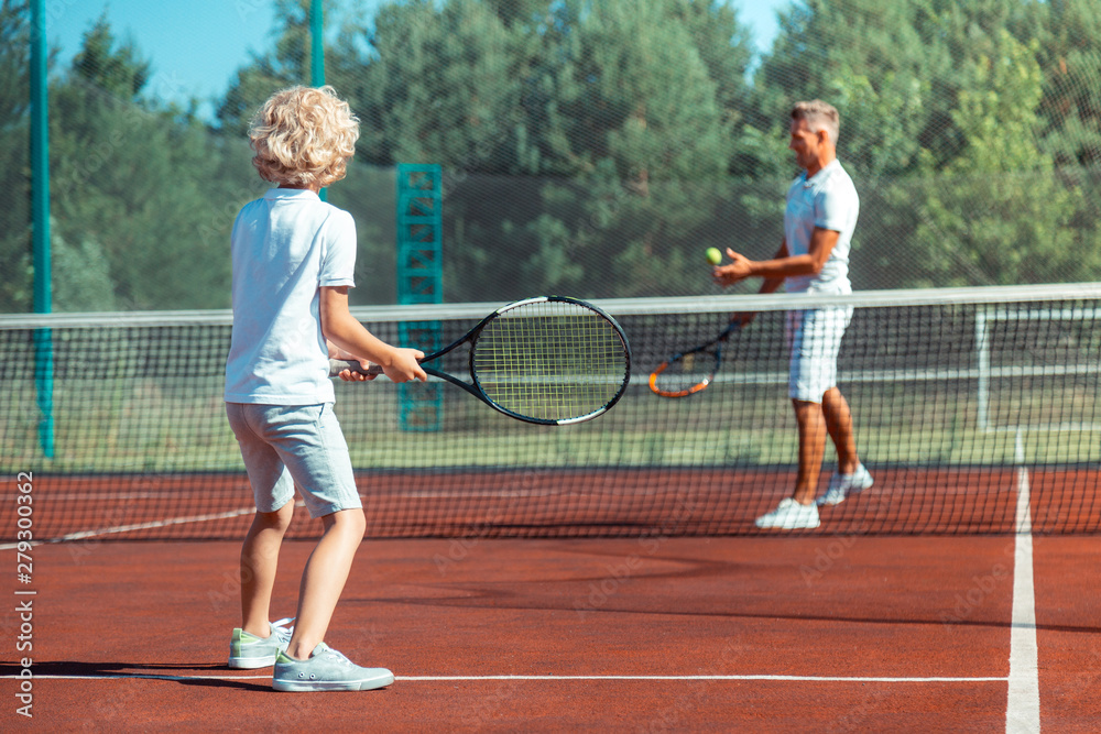 Father and son enjoying warm summer day playing tennis outside