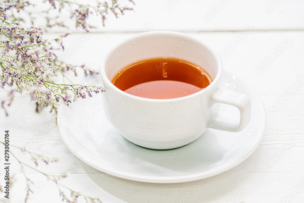 A cup of tea on white painted wood background with branch of small flower A cup of tea on white painted wood background with branch of small flower