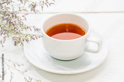 A cup of tea on white painted wood background with branch of small flower