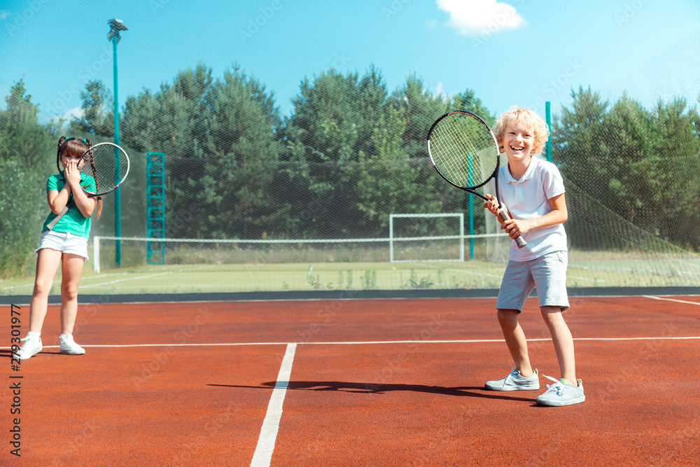 Cheerful brother feeling happy playing tennis with sister