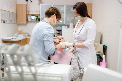 Doctor dentist and assistant doing dental operation of senior man patient in dental office. Dental fillings. Dental care for elder people.