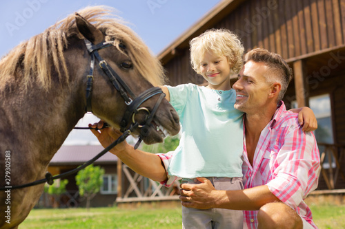 Father and son standing near good-looking brown horse
